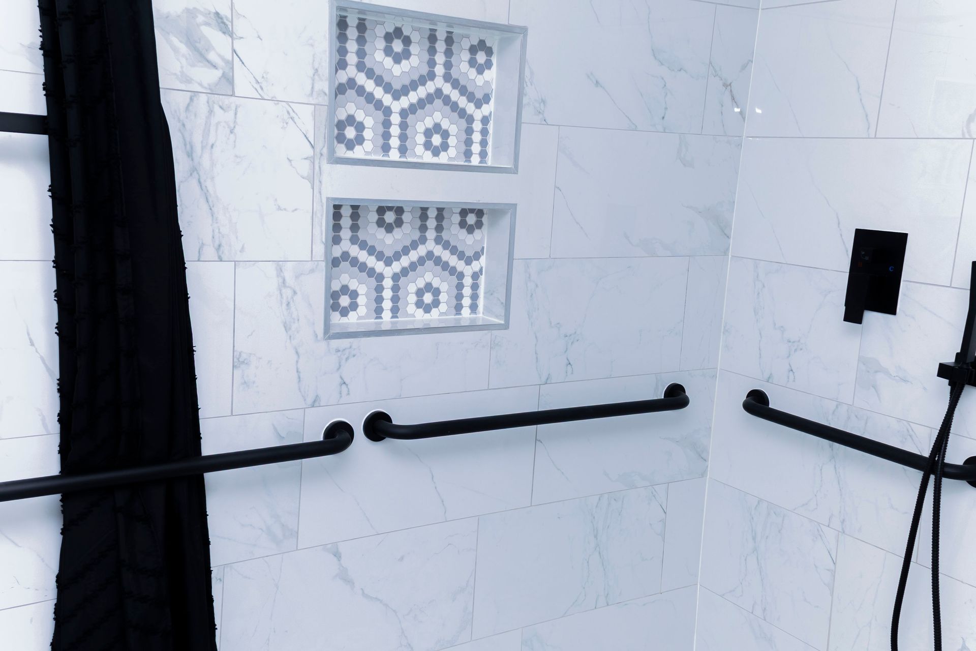 A modern white marble-tiled shower with black hardware, grab bars, and a stacked double niche with geometric tile.