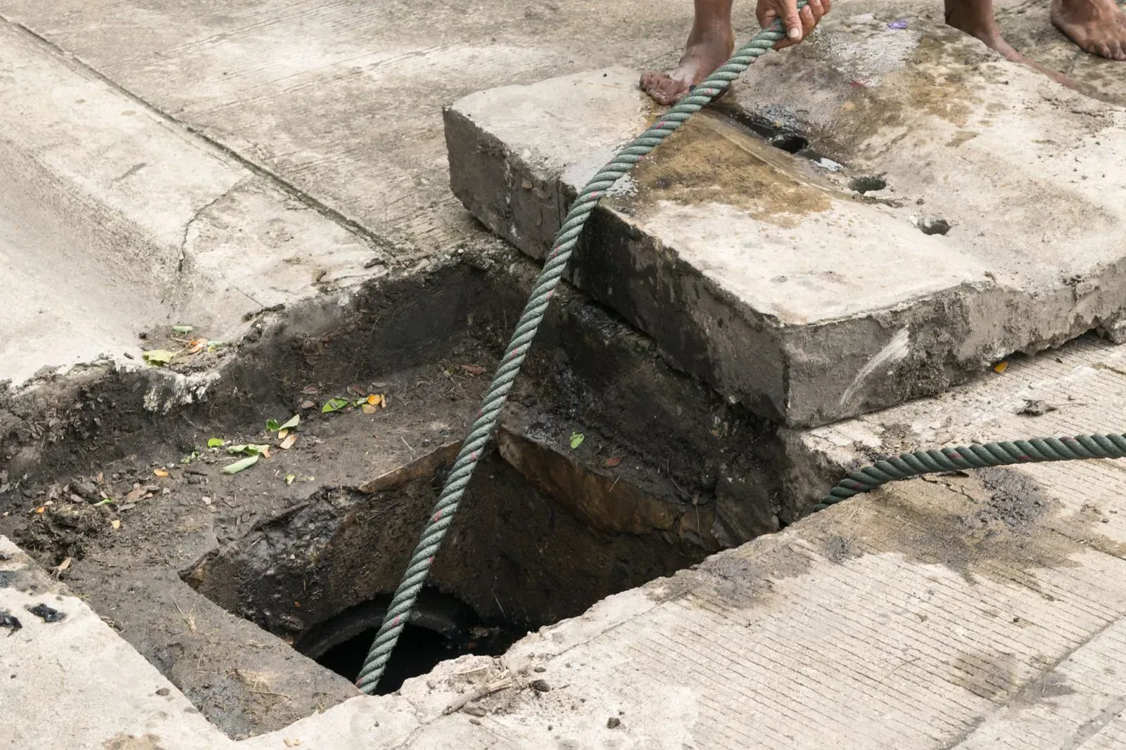 A person is holding a hose over a hole in the ground.