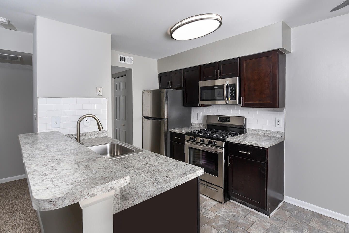 Kitchen in an apartment with stainless steel appliances, dark wood cabinets, and light gray walls.