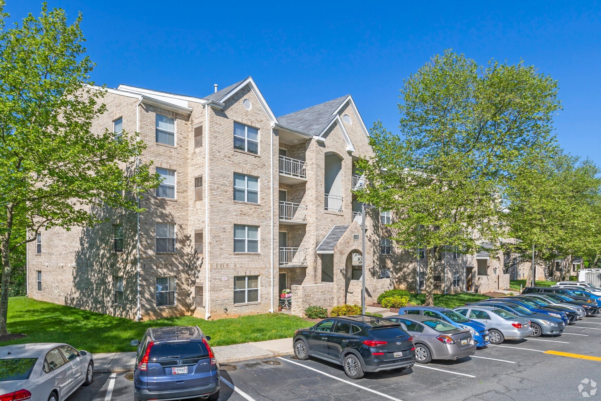 Exterior brick apartment building with multiple stories, green lawn, and parked cars.