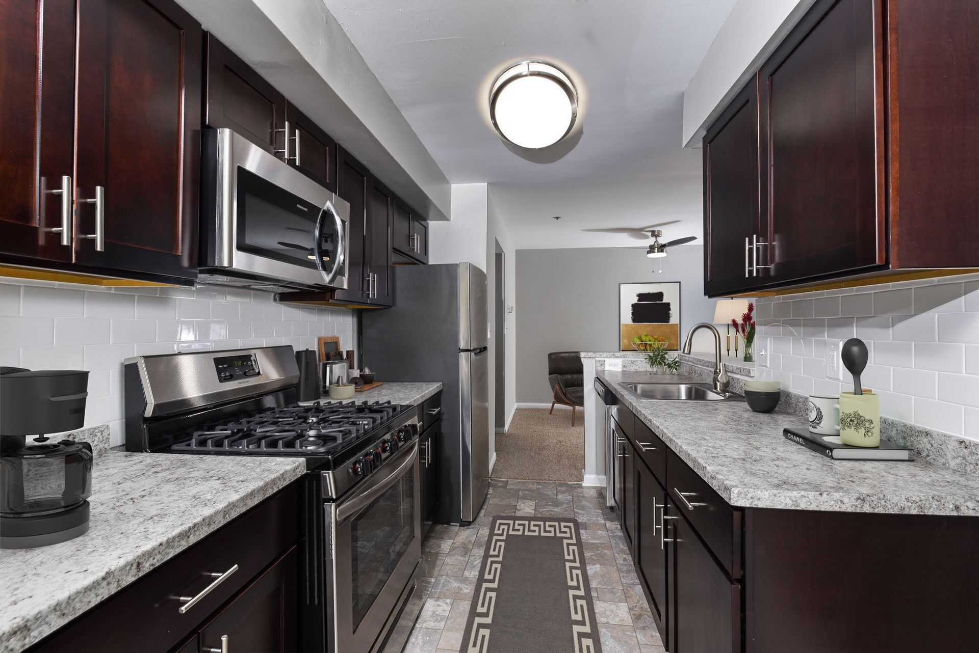 Modern galley kitchen with dark wood cabinets, stainless steel fridge, microwave, and double sink.
