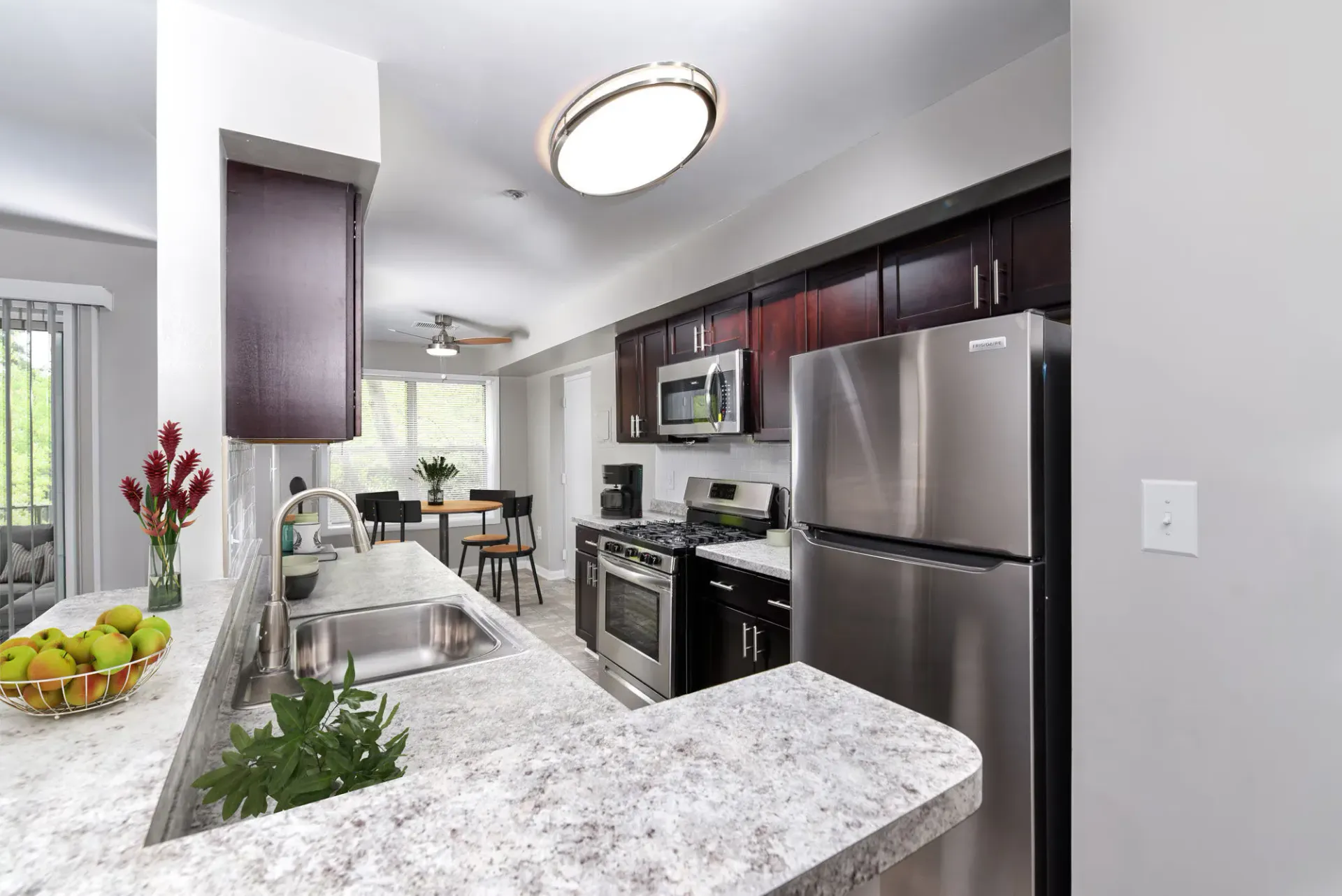 Modern apartment kitchen with stainless steel appliances, dark wood cabinets, and a curved granite countertop.