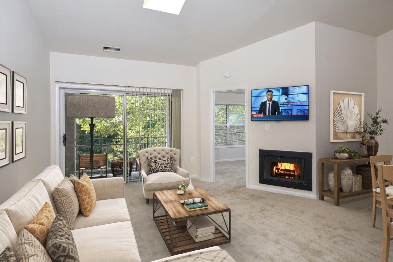 Living room with beige sofa, accent chair, fireplace, wall-mounted TV, and sliding glass door to balcony.