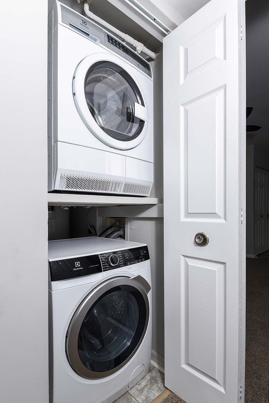 Stacked front-loading washer and dryer in a laundry closet with door open.