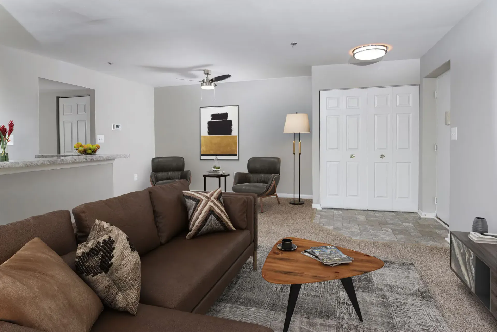 Living room in an apartment with a brown sofa, two gray chairs, and a wooden coffee table.