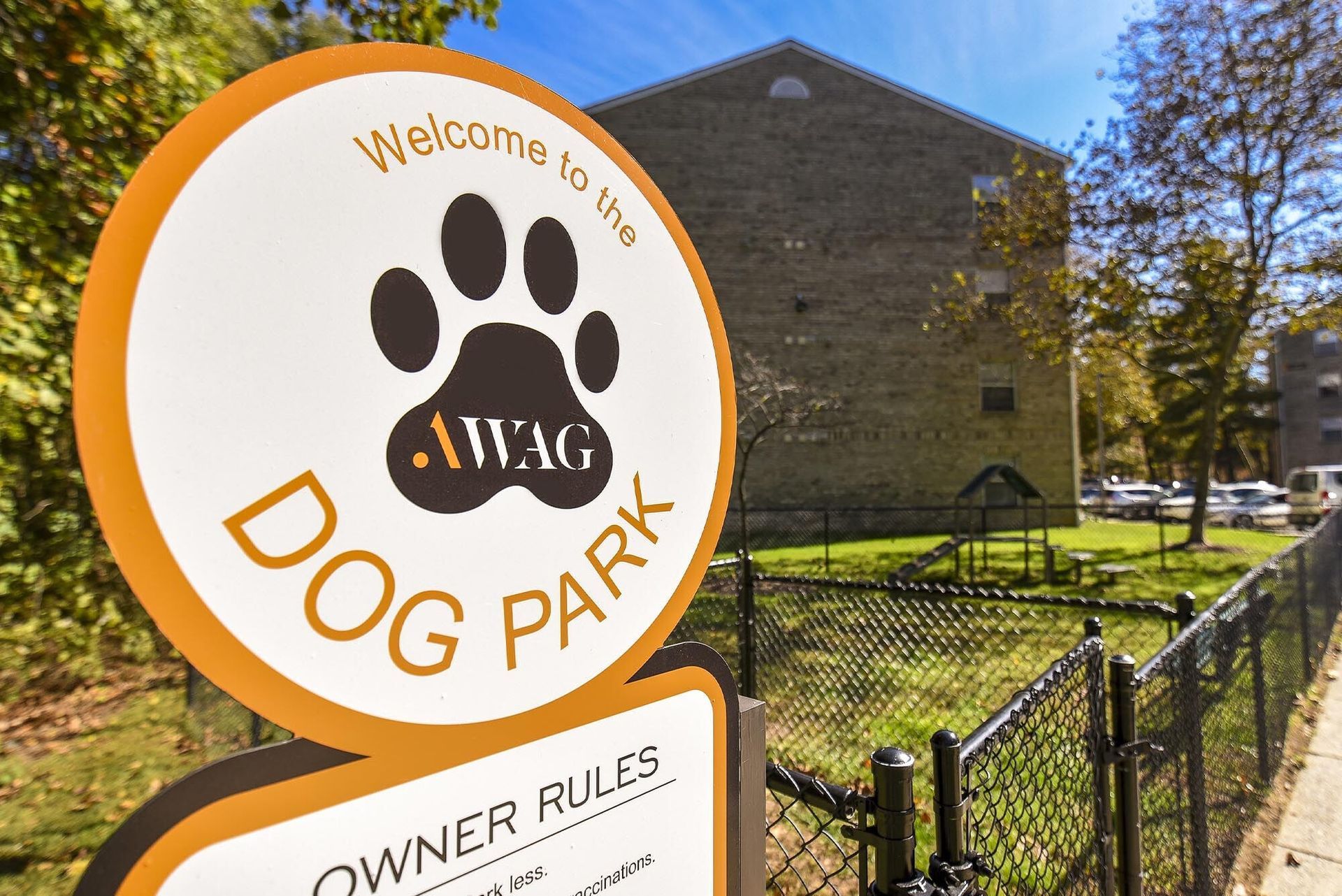 Circular dog park sign in foreground with apartment building and fence in background.
