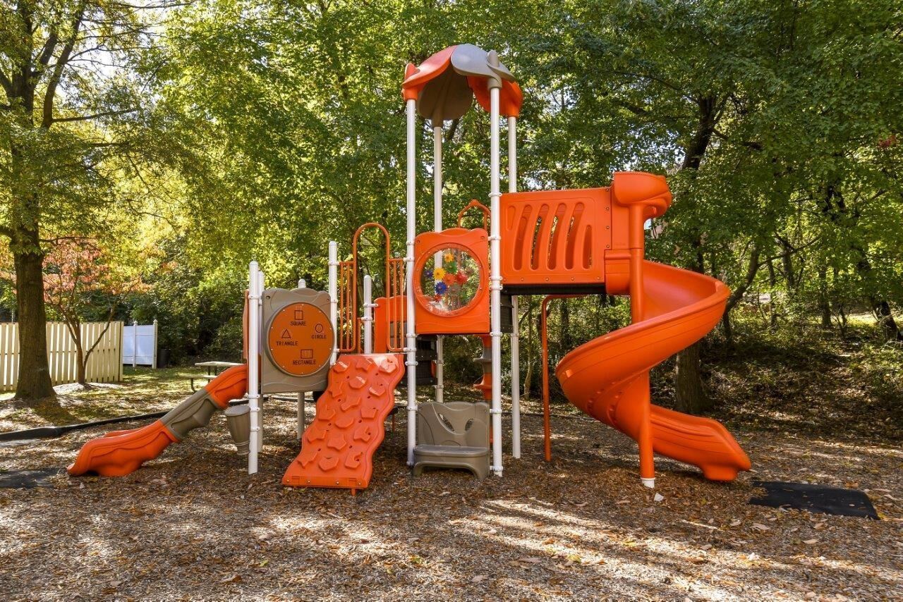 Orange playground with slides and climbing equipment in a wooded outdoor area.