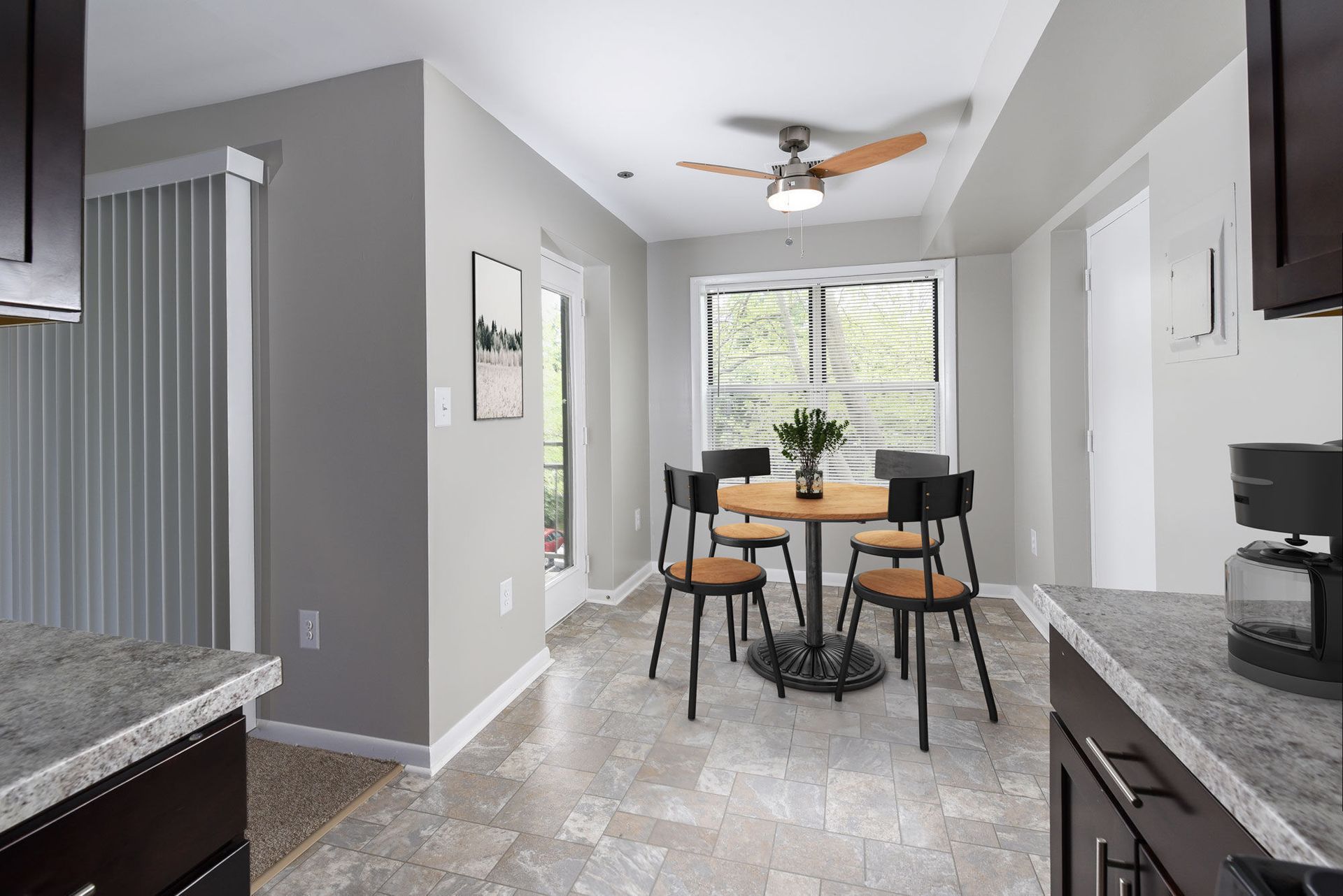 Dining area in an apartment with a round wood table, four chairs, and a ceiling fan near a large window.
