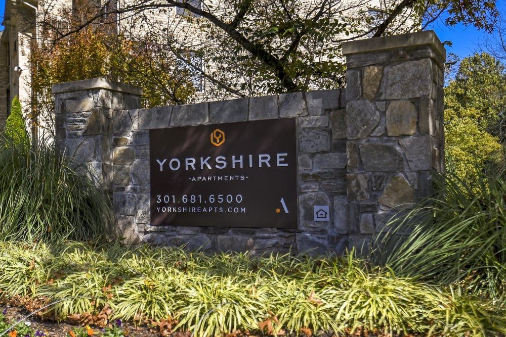 Stone entrance sign for Yorkshire Apartments on a stone wall with landscaping.