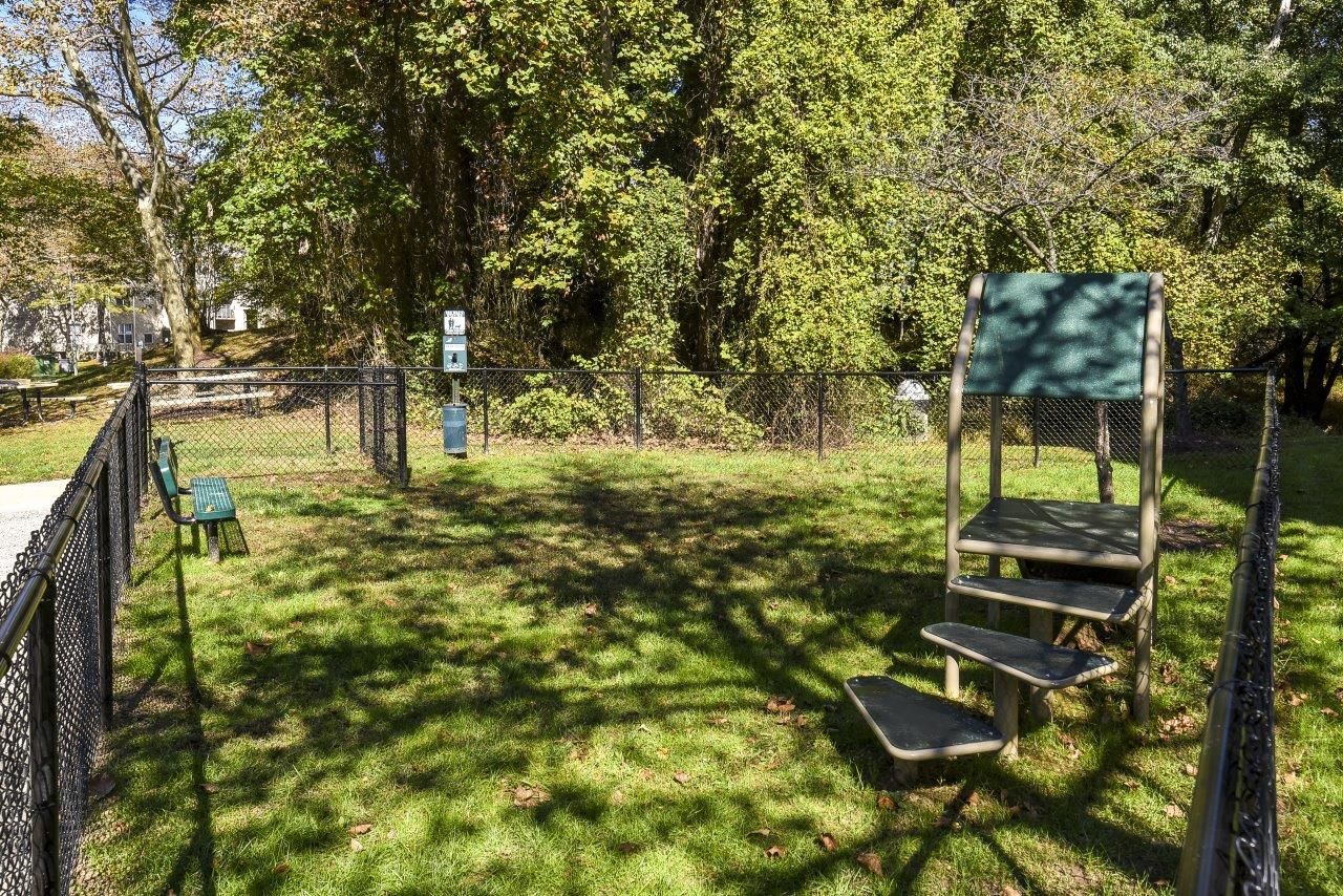 Fenced grassy playground area with a small climbing structure and bench.
