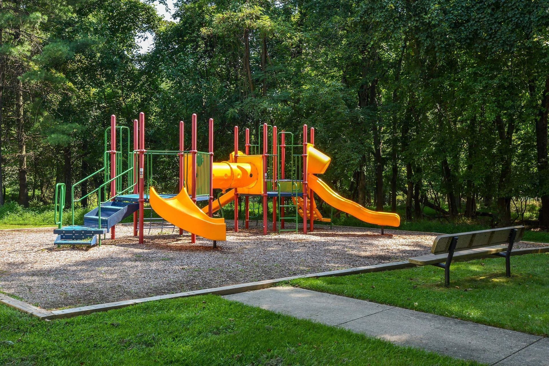 Colorful playground with orange slides and green posts in a shaded park.
