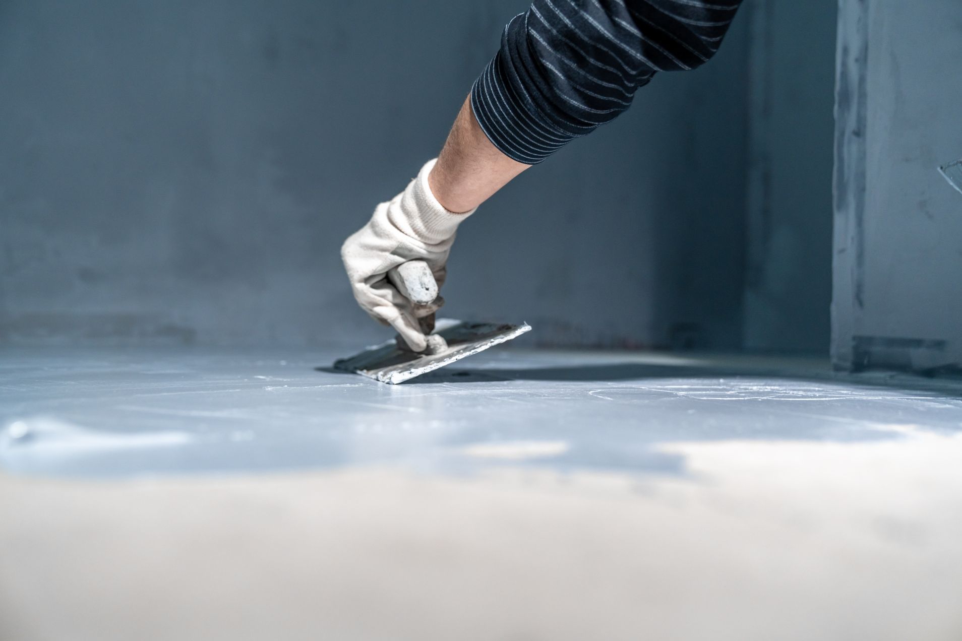 A Person Is Plastering a Floor with A Trowel — Affordable Tiling & Waterproofing in Kirwan, QLD