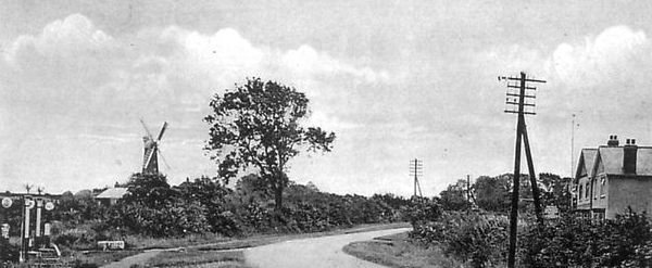 A black and white photo of a country road with a windmill in the background.
