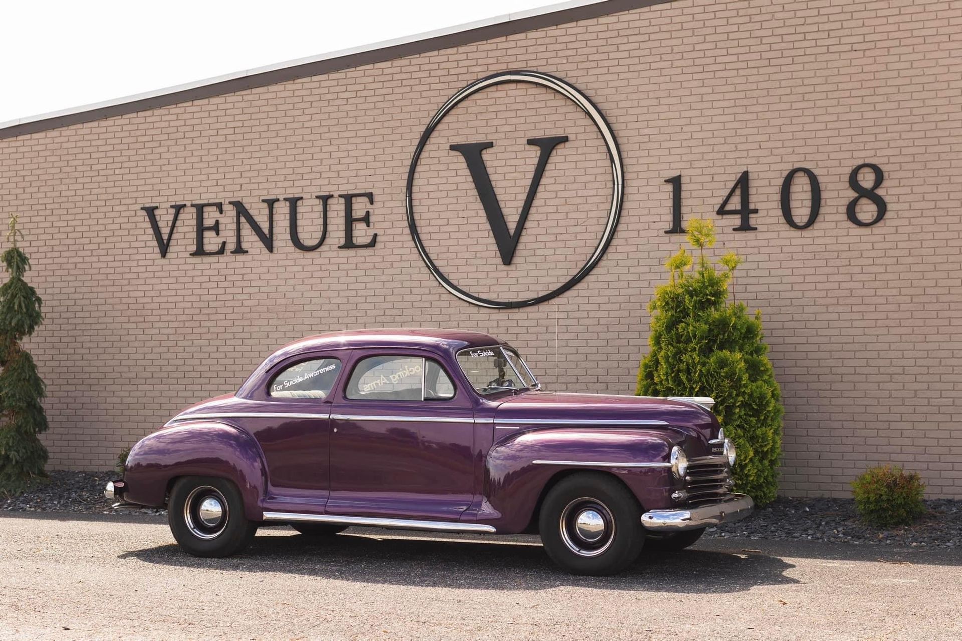 A purple car is parked in front of a building that says venue v 1408