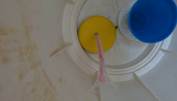 A clear, plastic tube with pink liquid passes through a yellow circular disc inside a white plastic container.