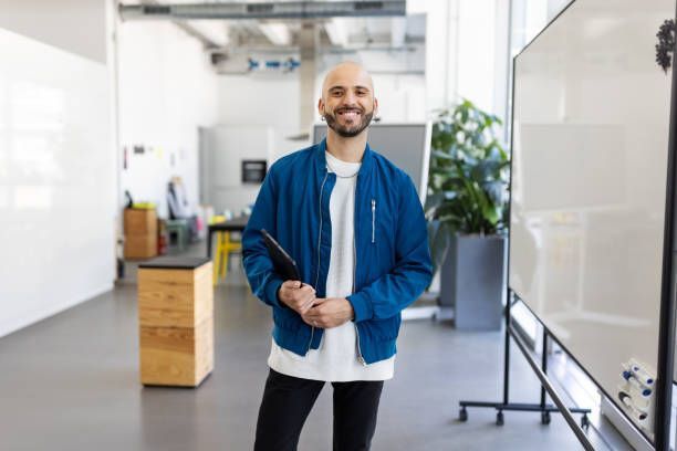 A man in a blue jacket is standing in front of a whiteboard in an office.