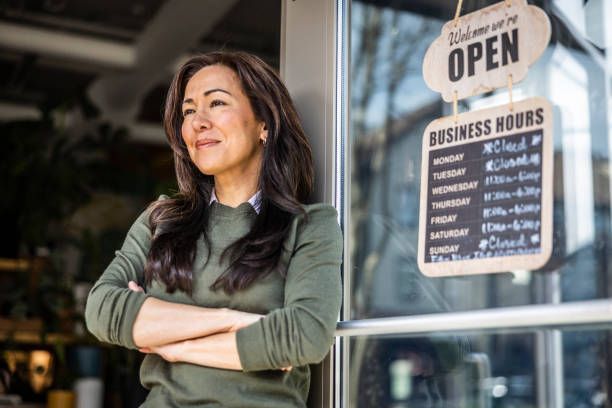 A woman is standing in front of a store with her arms crossed.