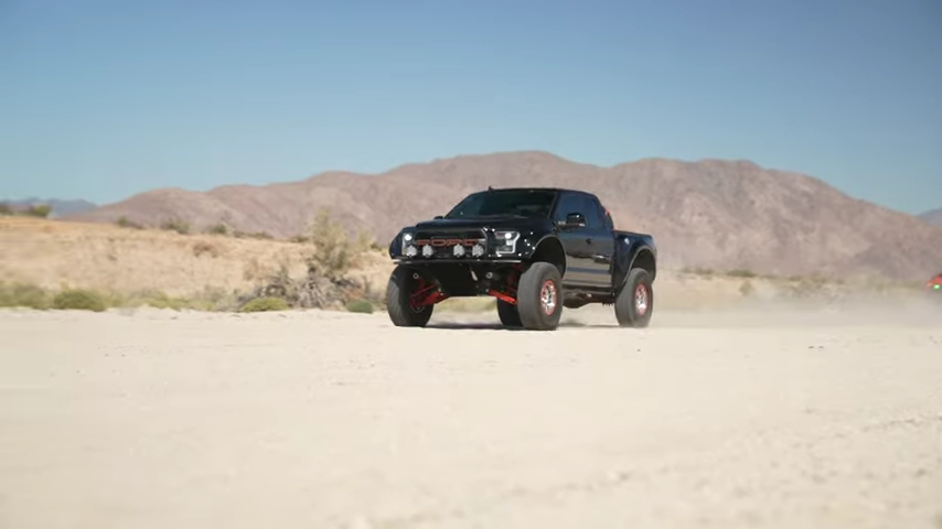A black truck is driving down a dirt road in the desert.