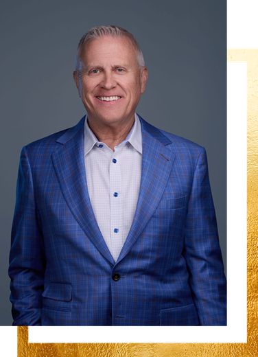 Man in blue plaid suit smiling, standing in front of a gray background.