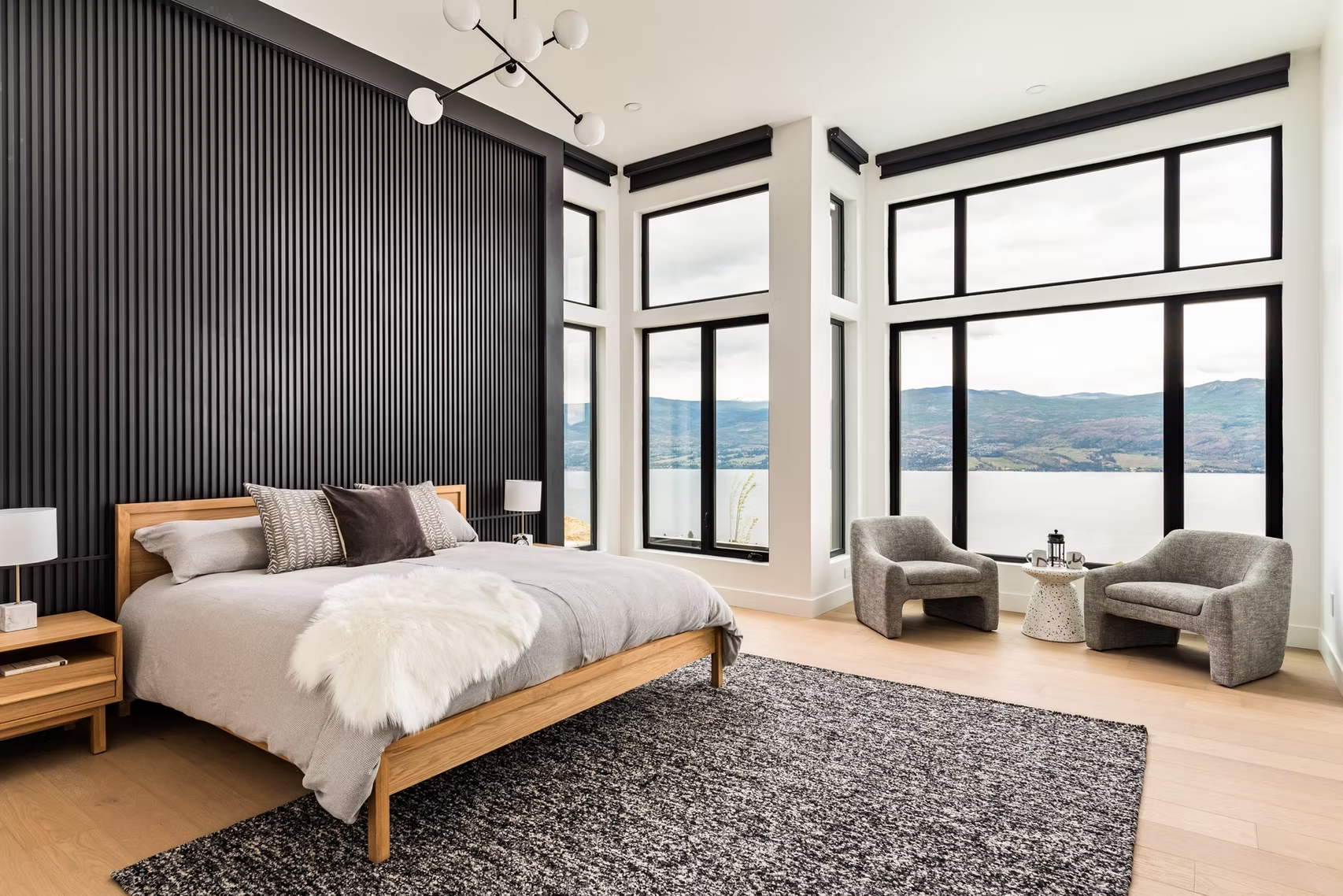 Modern bedroom with large windows, mountain view, gray bed, and two chairs on a patterned rug