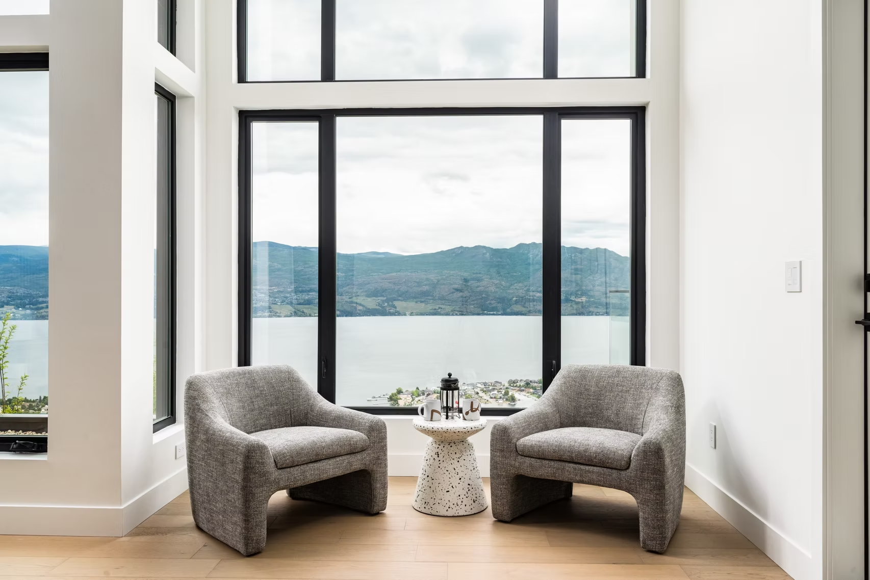 Modern lounge with two gray chairs and a small table overlooking a large window and water view