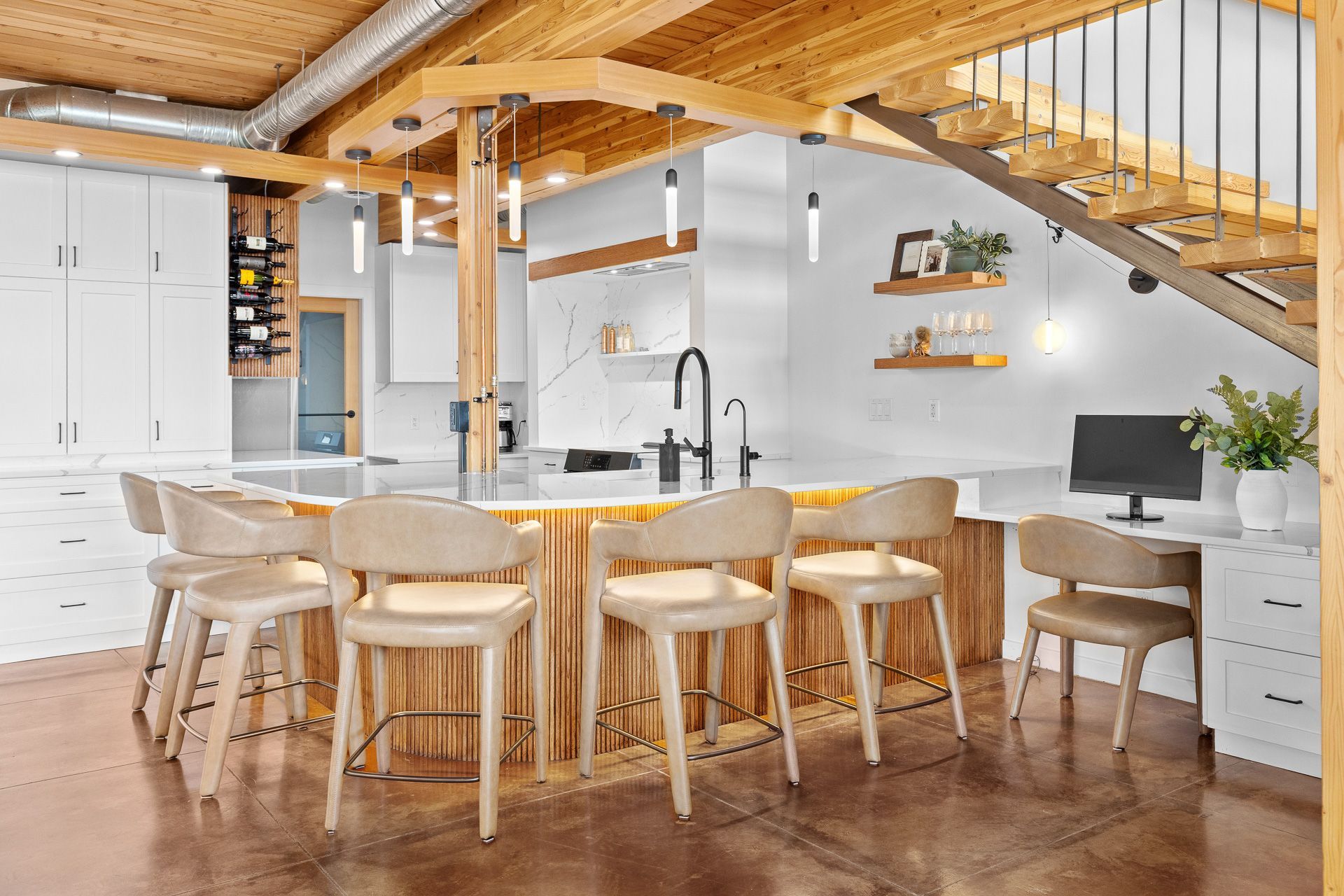 Bright modern kitchen with wooden beams, white island, stools, and open staircase in a loft interior