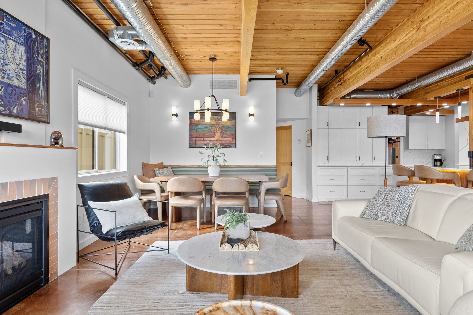 Bright modern living room with white sofa, fireplace, dining table, and exposed wood ceiling