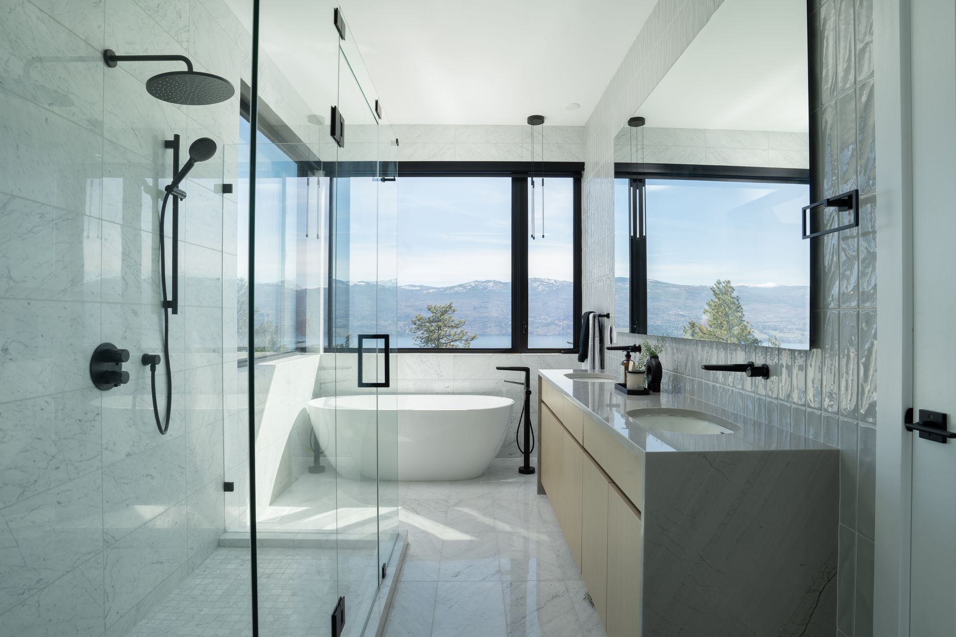 Modern glass-walled bathroom with freestanding tub, walk-in shower, and mountain view