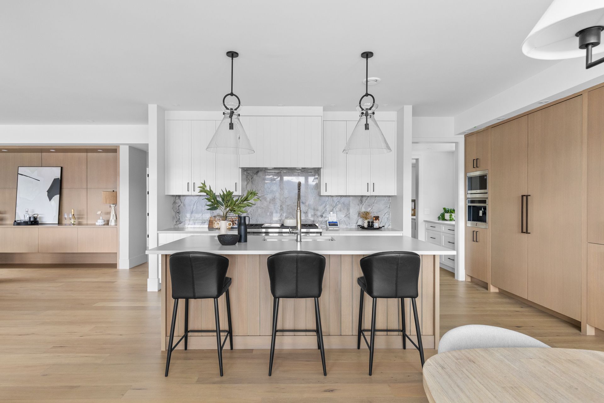 Modern open-plan kitchen with white cabinets, marble island, black stools, and wood floors