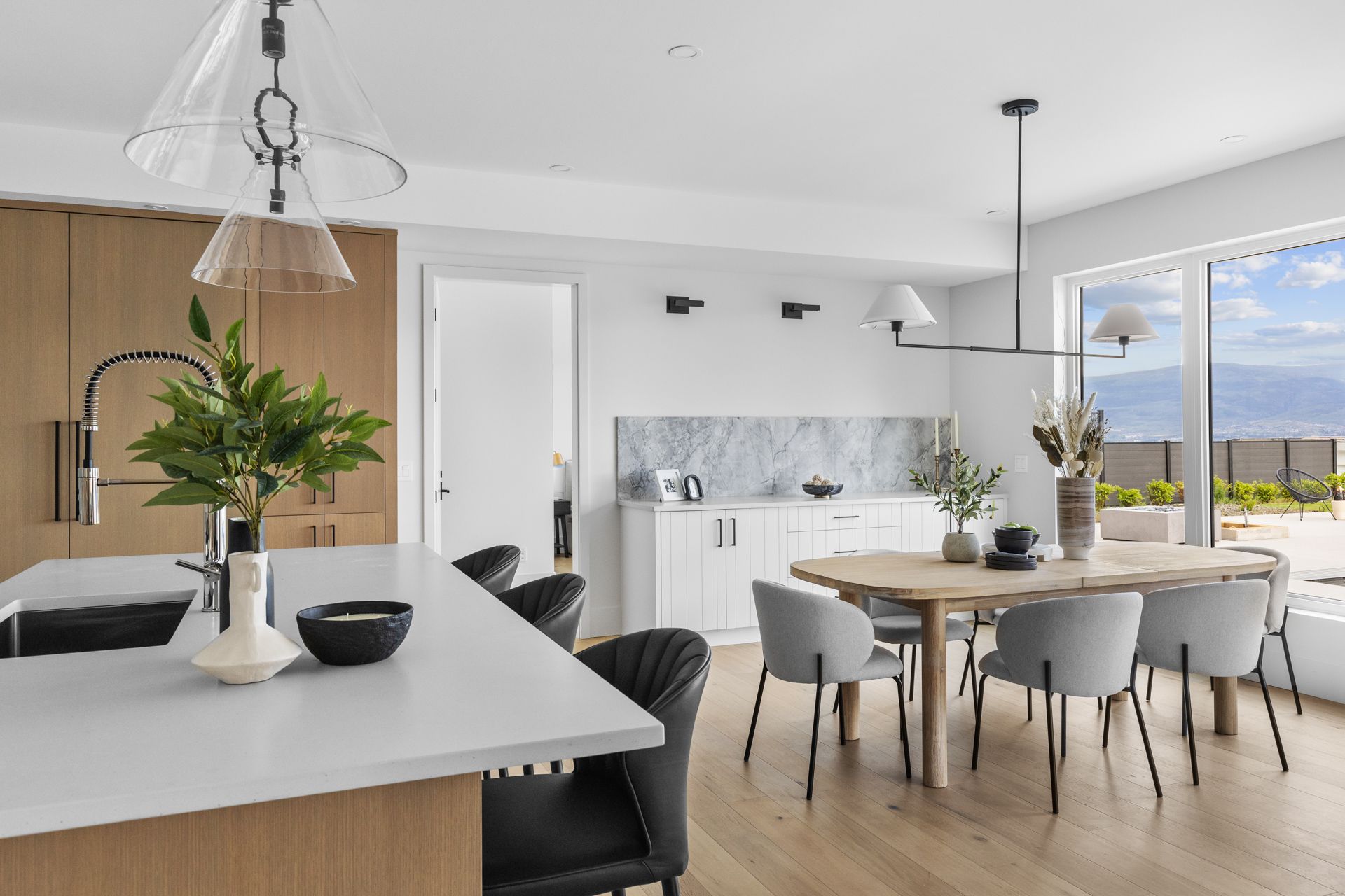 Bright modern kitchen and dining area with white cabinets, marble backsplash, and a view through large windows