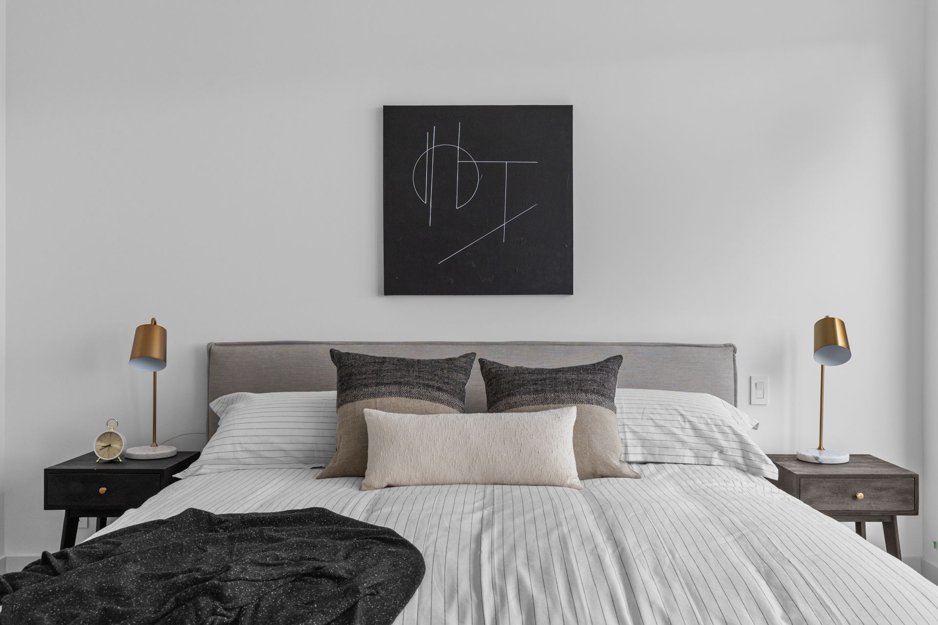 Minimalist bedroom with gray bed, white bedding, dark artwork, and bedside lamps
