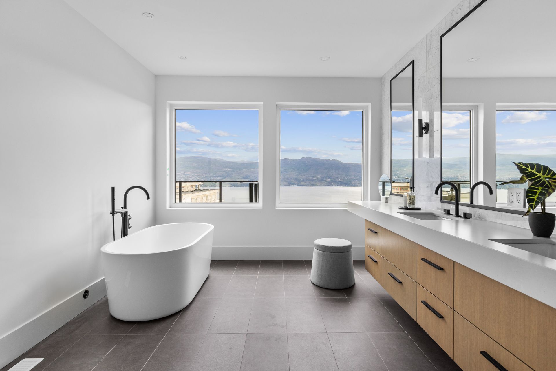 Modern bathroom with freestanding tub, double vanity, and large windows overlooking the water