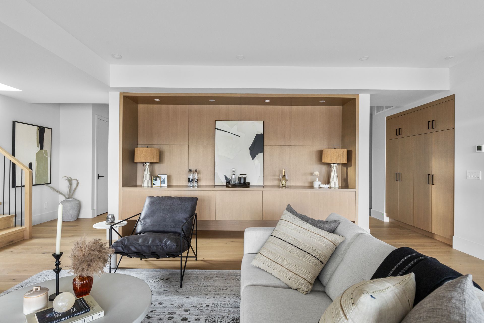 Modern living room with beige sectional, lounge chair, wood-paneled wall, and built-in shelving.
