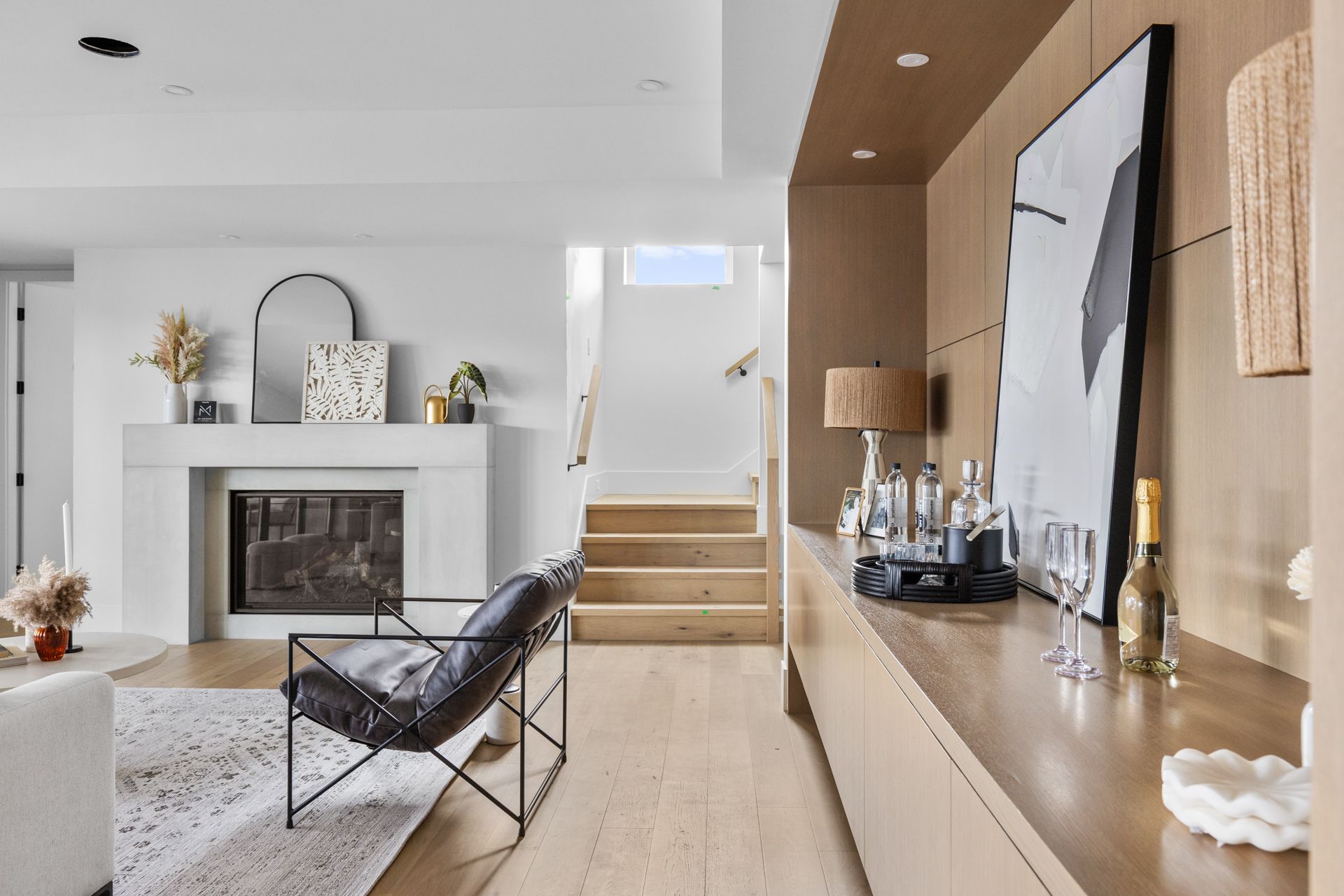 Bright modern living room with fireplace, black lounge chair, and wood-accented hallway and console table.