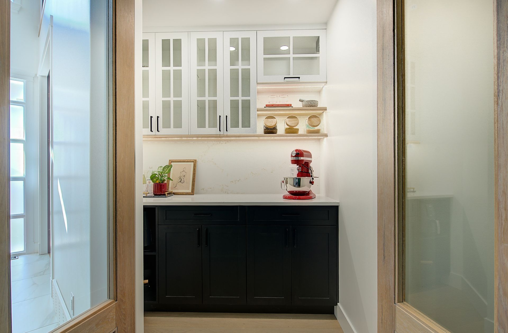 Small home bar nook with white cabinets, dark lower cabinet, and a red coffee maker between frosted glass doors
