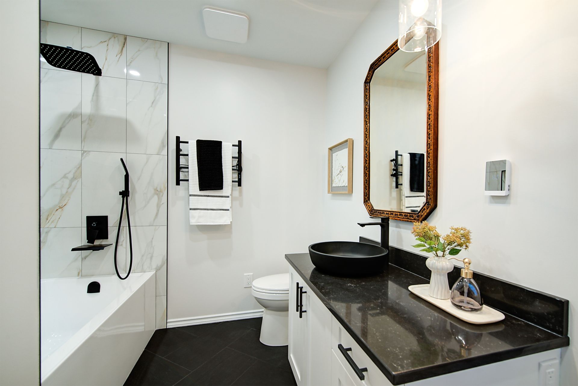 Modern bathroom with black marble vanity, glass shower, and white tile walls