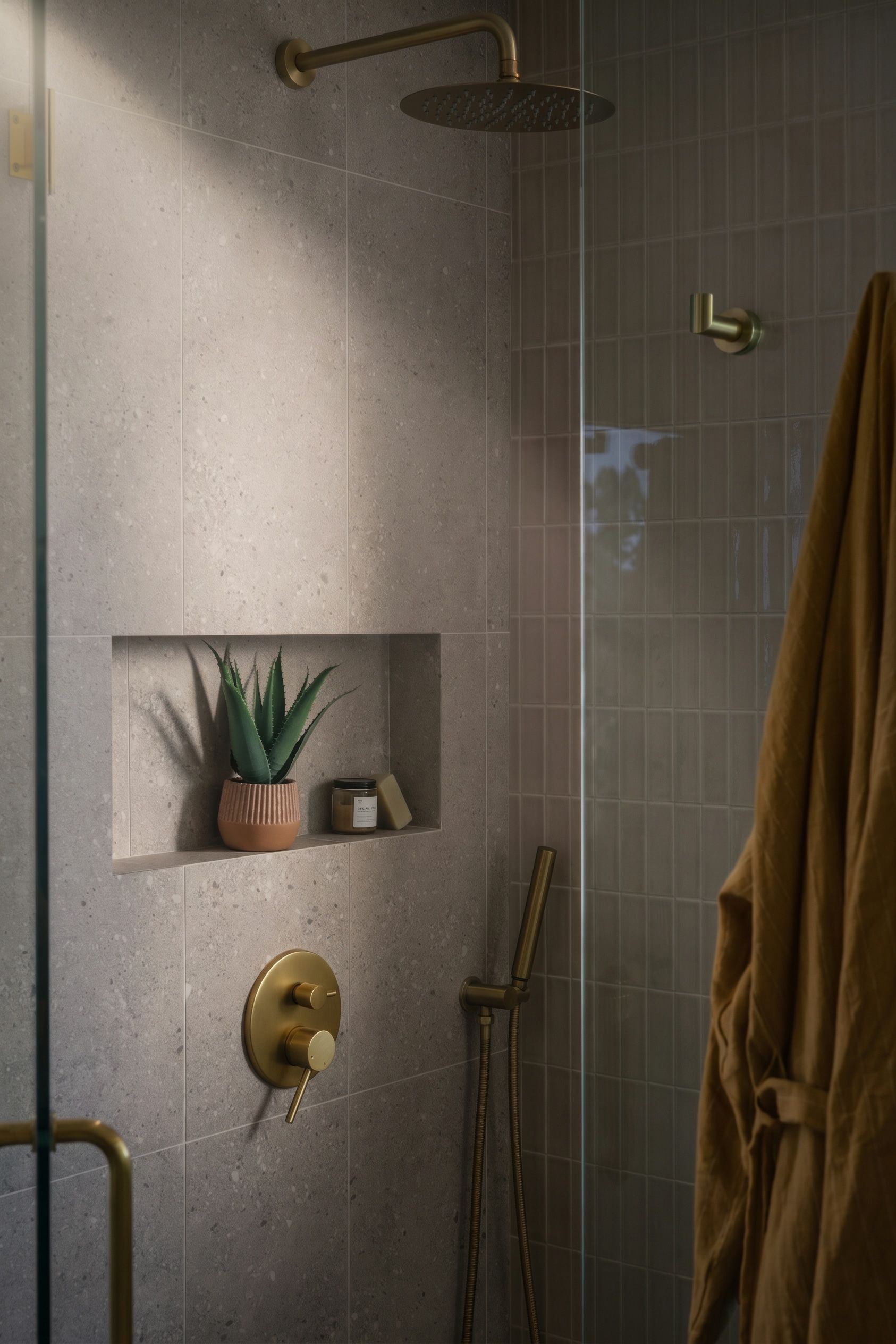 Tiled shower with brass fixtures, wall niche with plants and decor, and a tan towel hanging on the side.