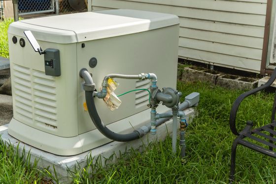 A generator is sitting in the grass in front of a house.