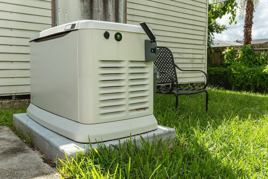 A generator is sitting in the grass in front of a house.