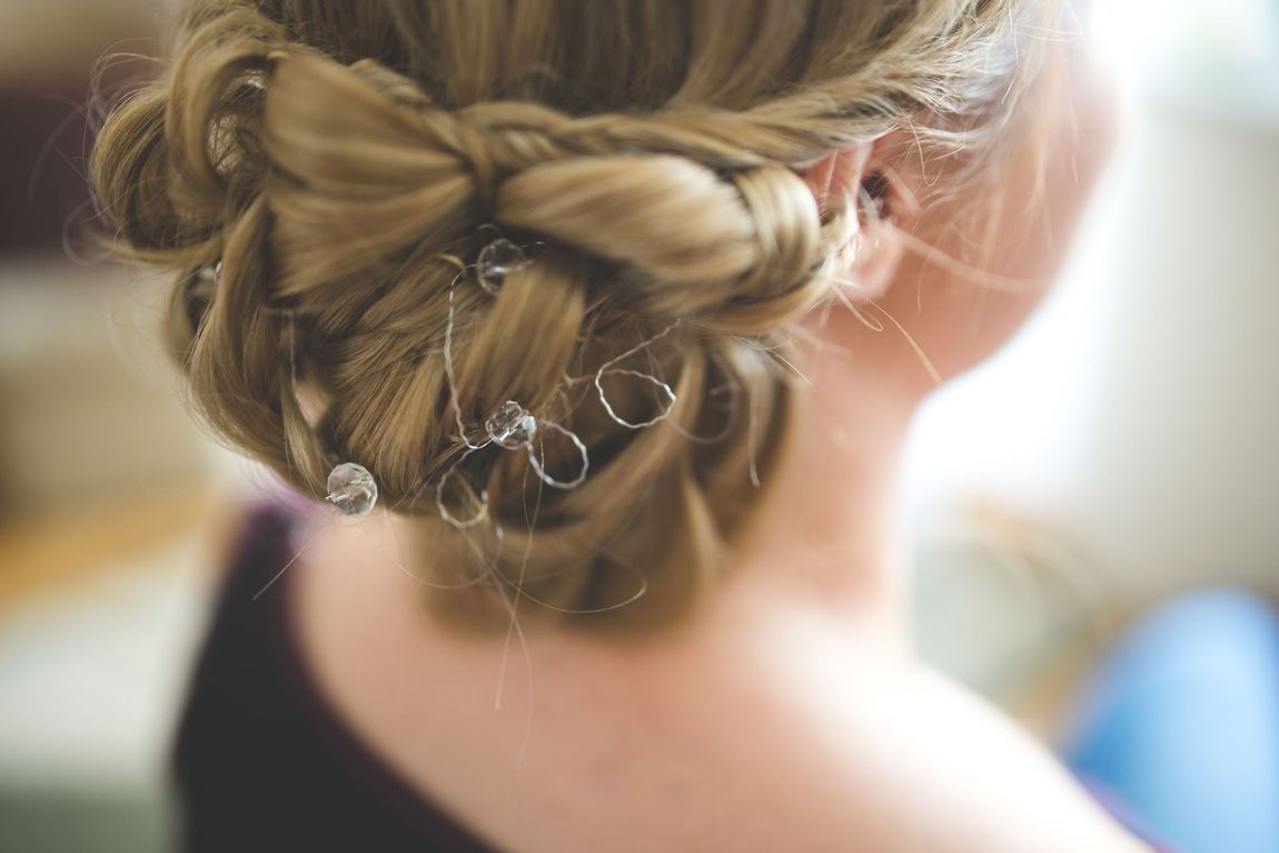 Intricate braided updo with small pearl hairpins, viewed from the back in soft focus