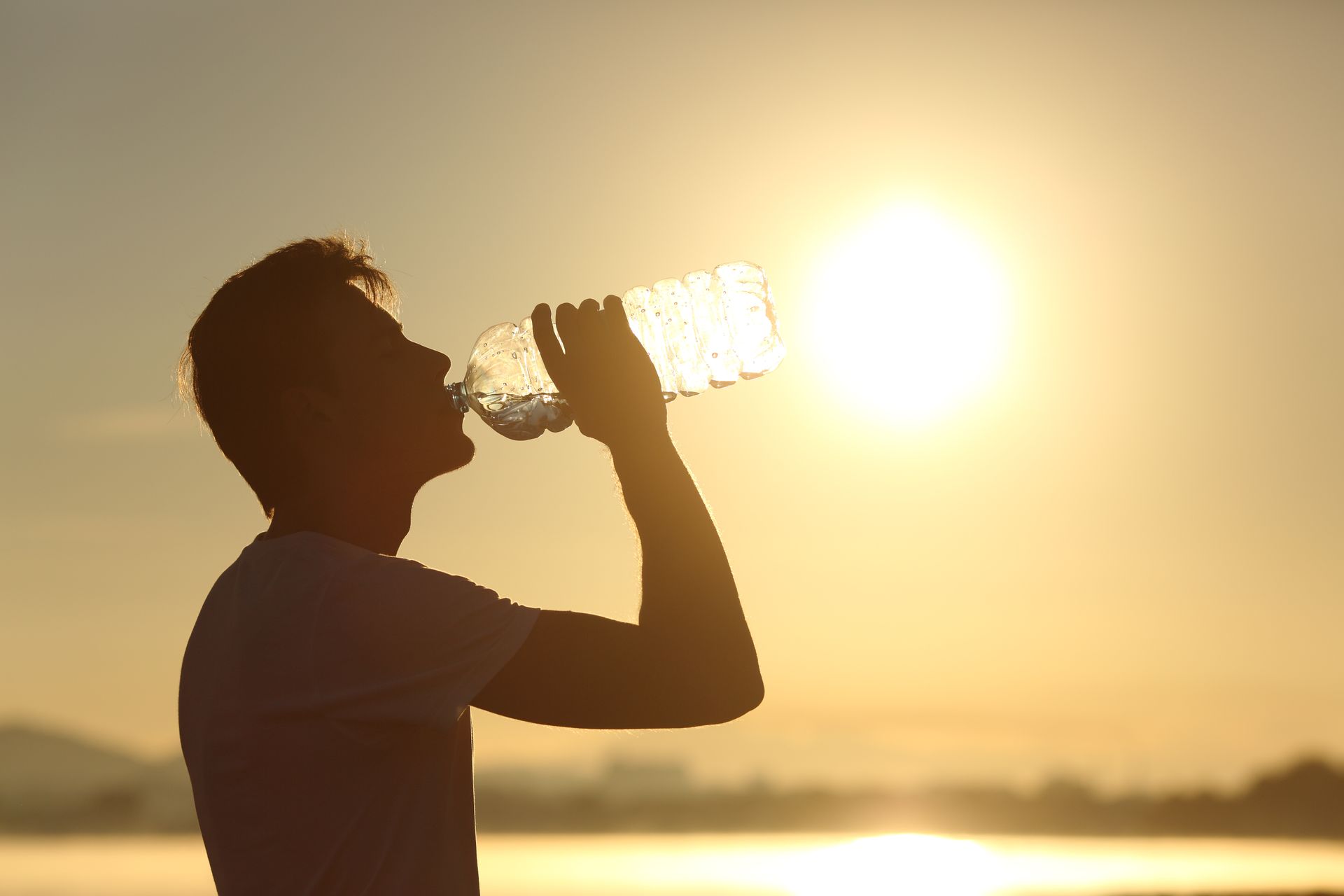 A man is drinking water from a bottle at sunset.