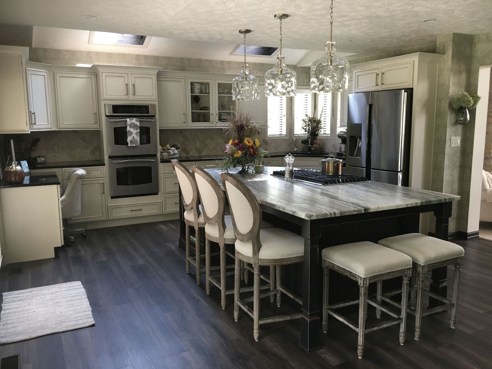 Kitchen with cream cabinets, large island with seating, stainless steel appliances, and dark wood-look floor.