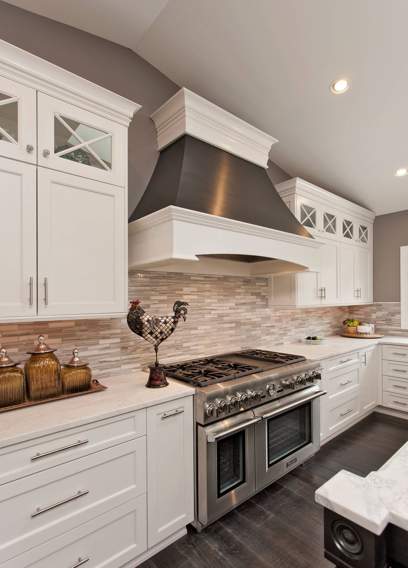 White kitchen with stainless steel oven, dark range hood, and stone backsplash.