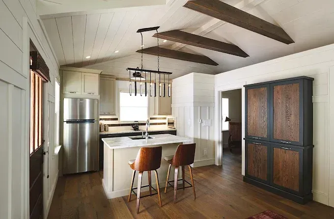 Kitchen with white walls, wood ceiling beams, stainless steel appliances, and brown leather bar stools.