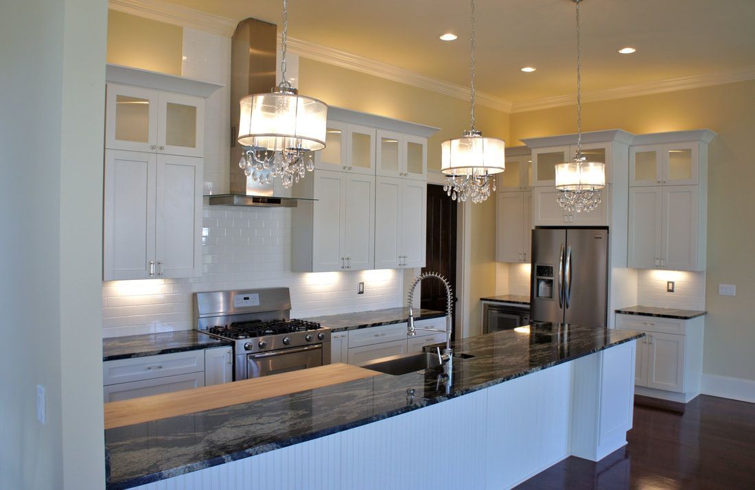 White kitchen with stainless steel appliances, dark countertops, and crystal chandeliers.