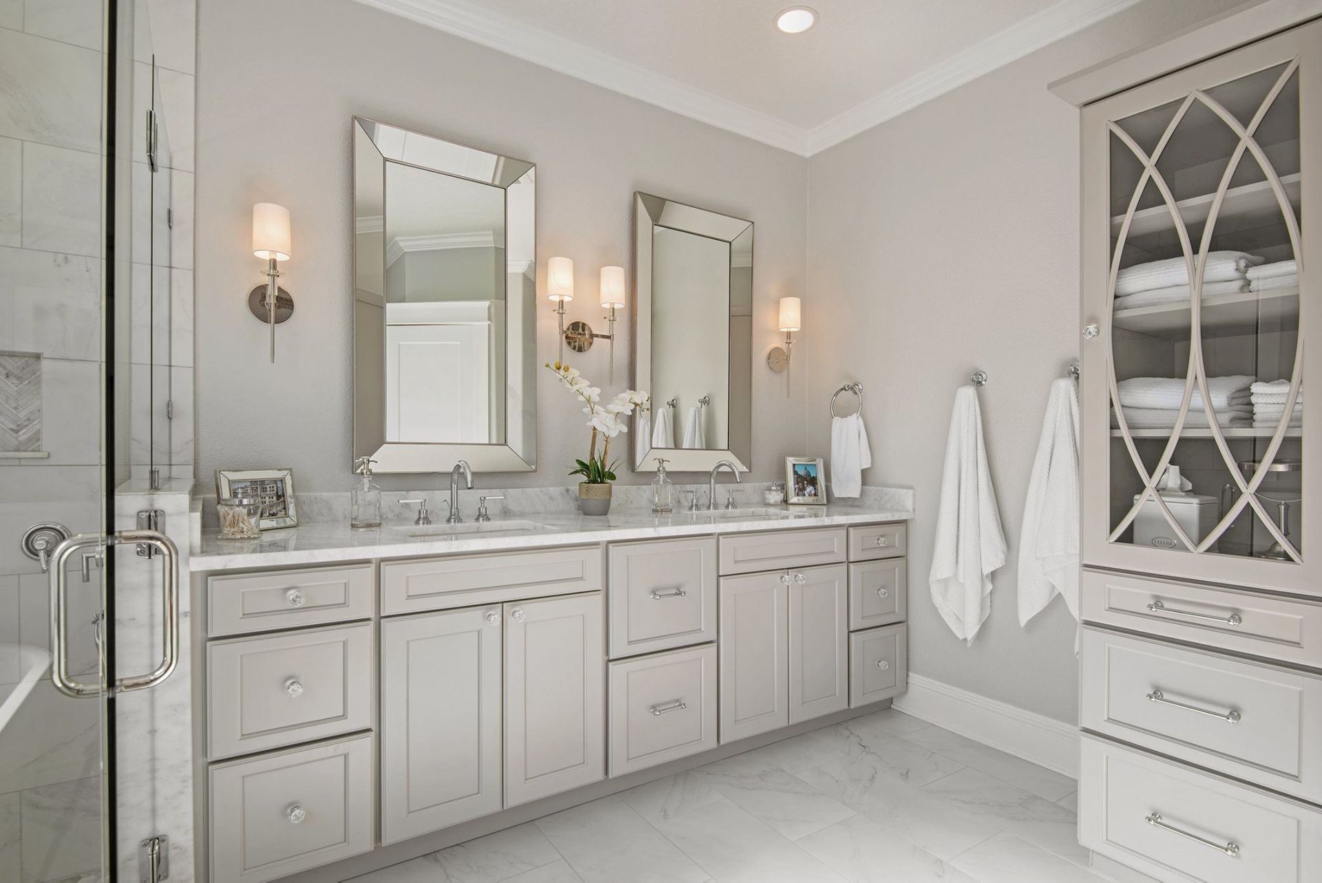 Bathroom with double vanity, large mirrors, built-in storage, and white marble accents.