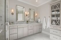 Bathroom with dual sinks, mirrors, and a gray vanity. Includes a glass shower and linen cabinet.