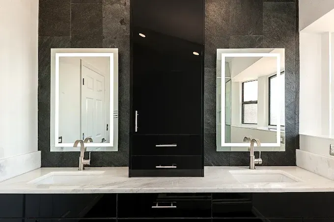 Modern bathroom with black vanity, marble countertop, two sinks, mirrors, and black cabinet.