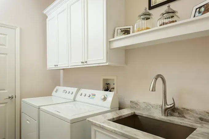 Laundry room with white appliances, cabinets, and a sink.