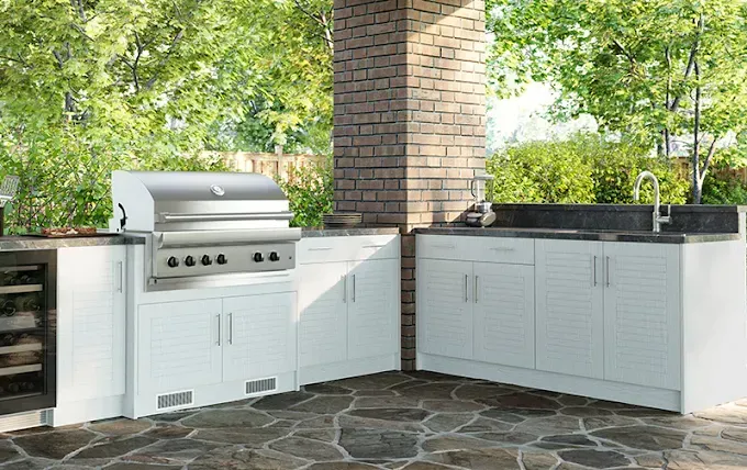 Outdoor kitchen with white cabinets, stainless steel grill, and stone patio.